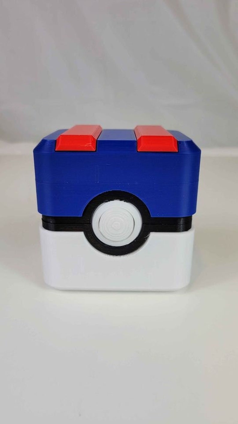May include: A blue and white 3D printed Pokemon Pokeball storage box with a red lid. The box is designed to look like a Pokeball.
