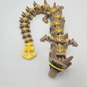 Pode incluir: Uma escultura castanha e amarela impressa em 3D com os textos "USN" e "NAVY". A escultura apresenta desenhos de &acirc;ncoras e estrelas. O design geral &eacute; uma representa&ccedil;&atilde;o estilizada de um tema militar.