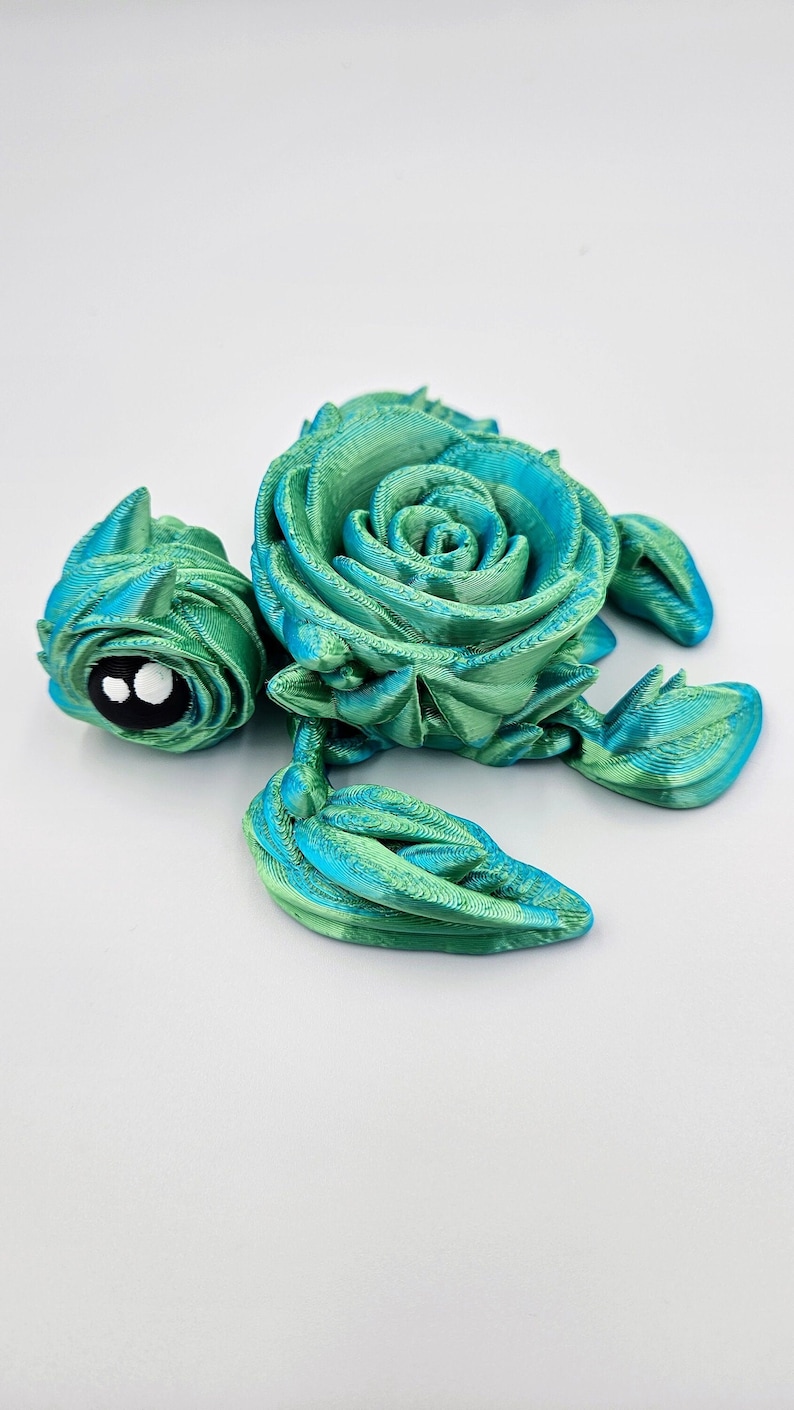 May include: A 3D printed sea turtle figurine with a green and blue color gradient. The turtle's shell is shaped like a rose.