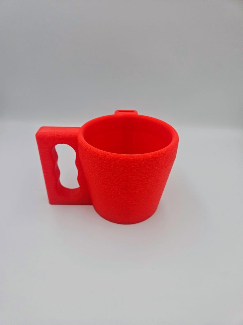 Pu&ograve; includere: Una tazza rosso vivo con superficie strutturata. Ha un manico rettangolare con apertura curva e una piccola cresta sul bordo. Progettata per bevande.