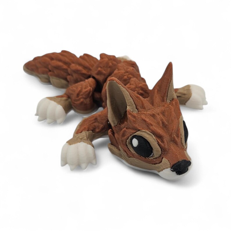 Peut inclure: Sculpture imprim&eacute;e en 3D d'un renard stylis&eacute; dans des tons de marron, beige et blanc. Le renard est couch&eacute;, les pattes tendues. La sculpture pr&eacute;sente une texture d&eacute;taill&eacute;e et de grands yeux noirs.