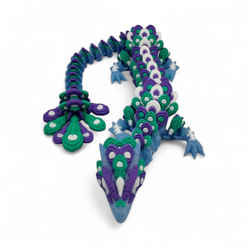May include: A colorful, articulated dragon sculpture in shades of blue, green, purple, and white. The dragon's body is segmented, with a detailed head and tail. The design features a peacock feather-like pattern.