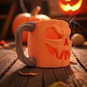 Pode incluir: Caneca de cer&acirc;mica laranja em forma de ab&oacute;bora de Halloween com um rosto esculpido. A caneca tem uma al&ccedil;a cinza e fica em uma superf&iacute;cie de madeira com folhas. Uma ab&oacute;bora iluminada e uma teia de aranha est&atilde;o no fundo, criando um tema de Halloween.