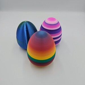 May include: Three decorative Easter eggs. One is blue, one is striped pink and purple, and one is a rainbow gradient with green and yellow stripes.