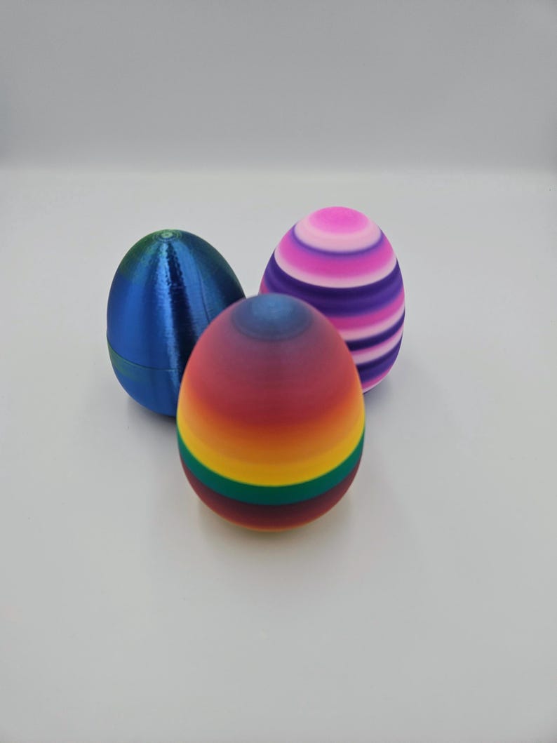 May include: Three decorative Easter eggs. One is blue, one is striped pink and purple, and one is a rainbow gradient with green and yellow stripes.