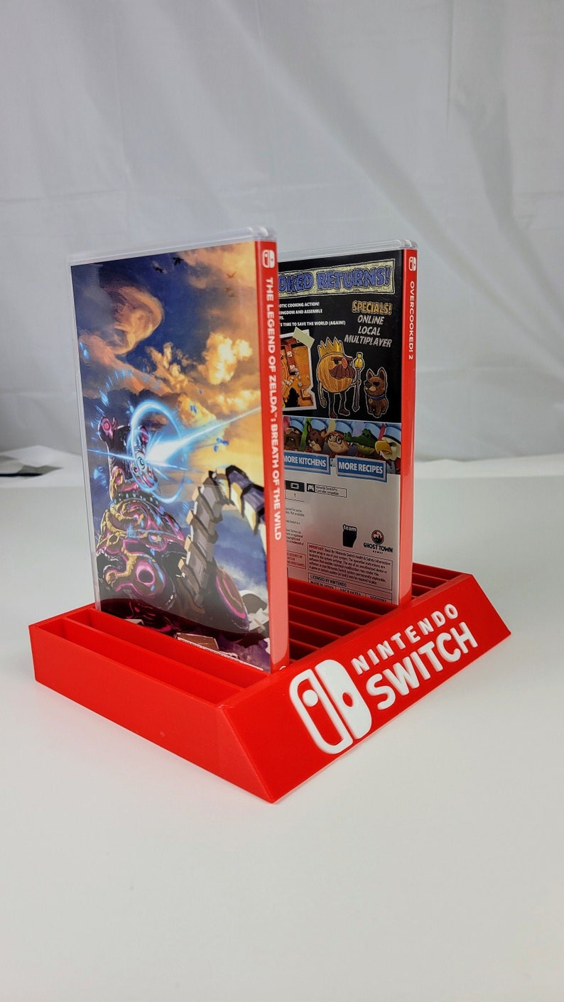 May include: A red Nintendo Switch game display stand with two game cases. The game cases are for "The Legend of Zelda: Breath of the Wild" and "Overcooked! 2".