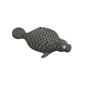Puede incluir: Figura de foca gris segmentada con un patr&oacute;n texturizado en forma de escamas. La foca tiene una cabeza redonda con peque&ntilde;os ojos blancos y una peque&ntilde;a aleta caudal. El objeto es decorativo.