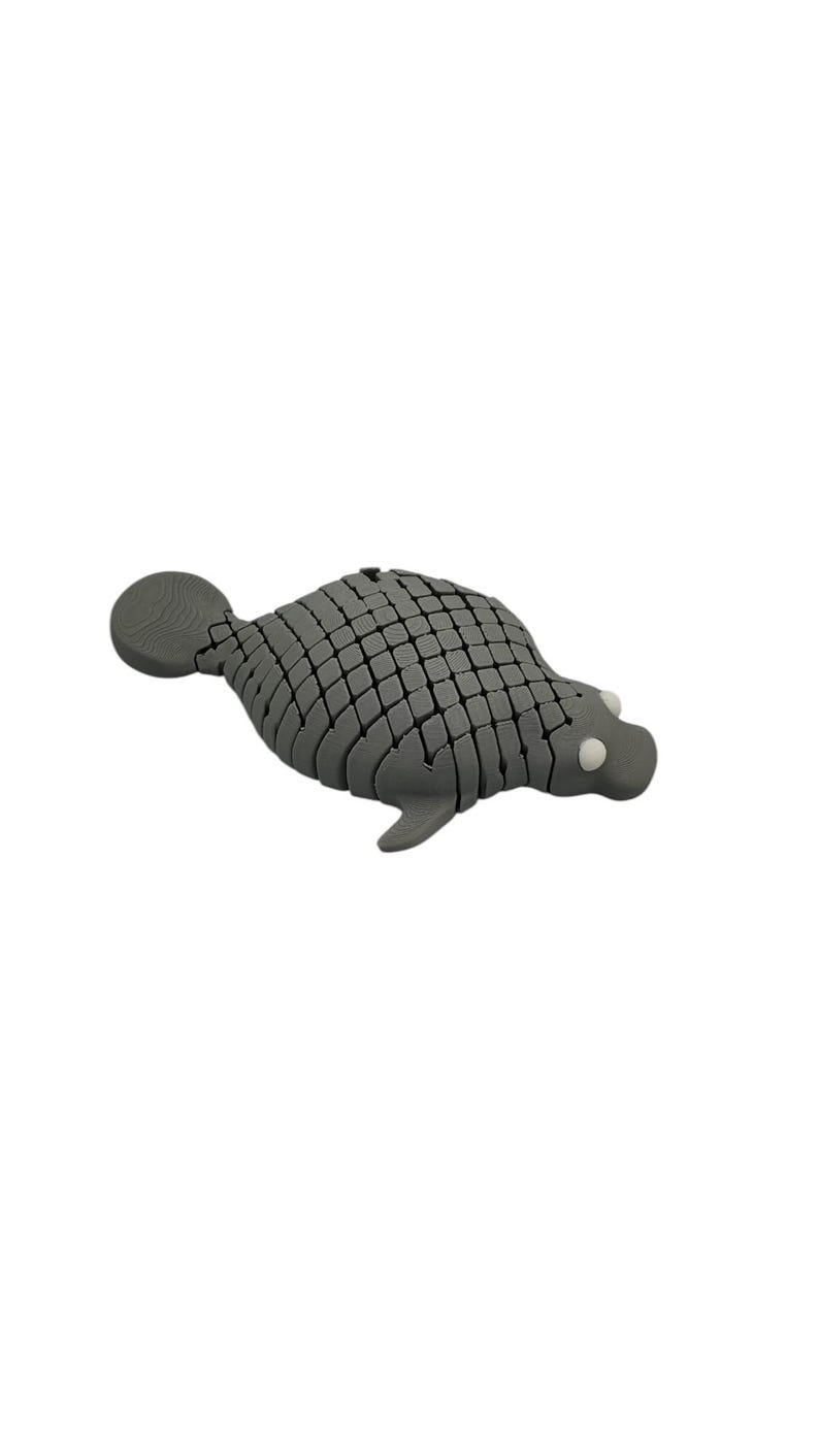 Puede incluir: Figura de foca gris segmentada con un patr&oacute;n texturizado en forma de escamas. La foca tiene una cabeza redonda con peque&ntilde;os ojos blancos y una peque&ntilde;a aleta caudal. El objeto es decorativo.