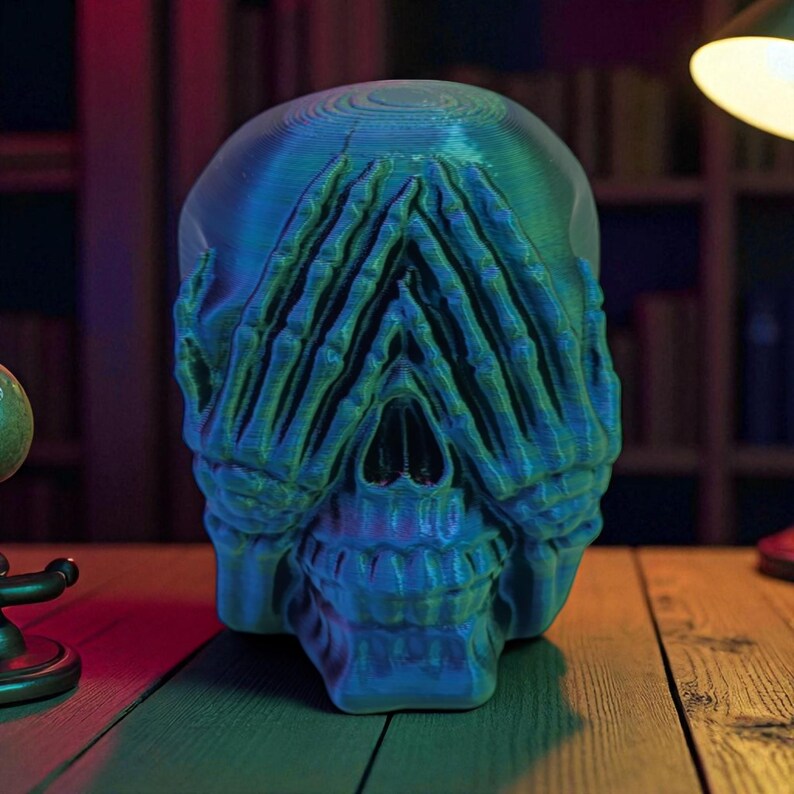 Op de afbeelding: Een blauwgroene schedelsculptuur met handen die de ogen bedekken. De schedel heeft een gedetailleerd ontwerp en is geplaatst op een houten oppervlak. De sculptuur wordt verlicht met blauw en groen licht.
