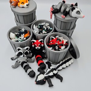 May include: A collection of gray trash cans with various animal figurines, including a fox, opossum, raccoon, red panda, and skunk. The trash cans are filled with colorful debris. The animals are in various poses, some on top of the cans.