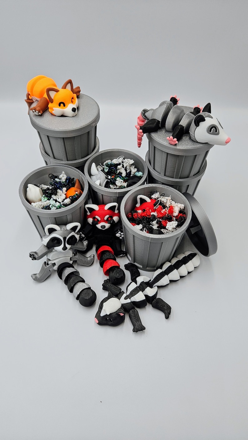 May include: A collection of gray trash cans with various animal figurines, including a fox, opossum, raccoon, red panda, and skunk. The trash cans are filled with colorful debris. The animals are in various poses, some on top of the cans.