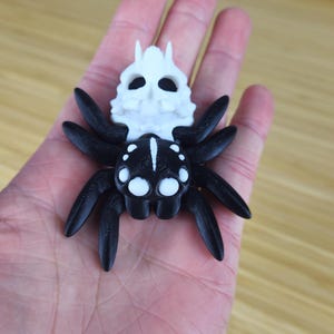 Puede incluir: Una ara&ntilde;a impresa en 3D en blanco y negro con una cabeza en forma de calavera. La ara&ntilde;a tiene ocho patas y una calavera blanca con ojos negros.
