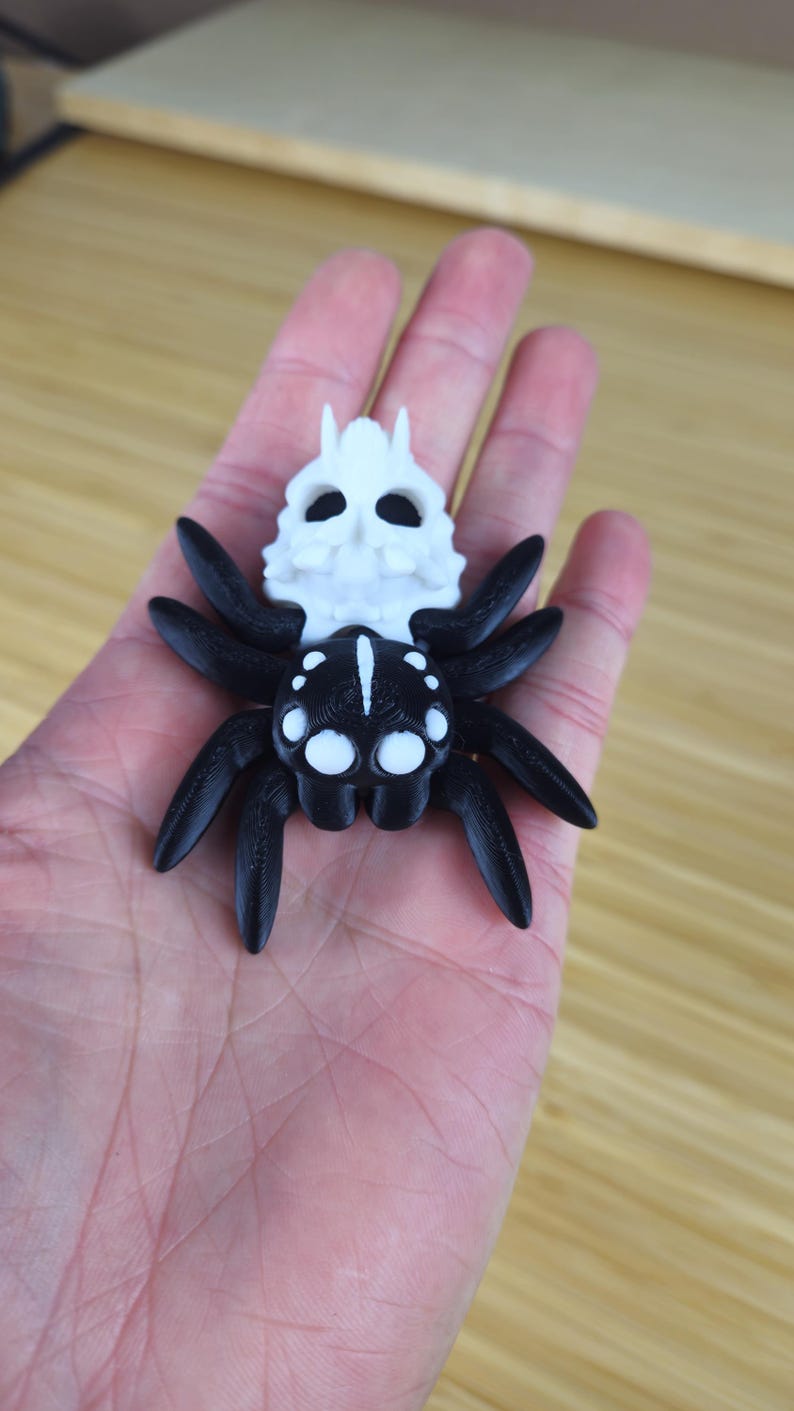 Puede incluir: Una ara&ntilde;a impresa en 3D en blanco y negro con una cabeza en forma de calavera. La ara&ntilde;a tiene ocho patas y una calavera blanca con ojos negros.
