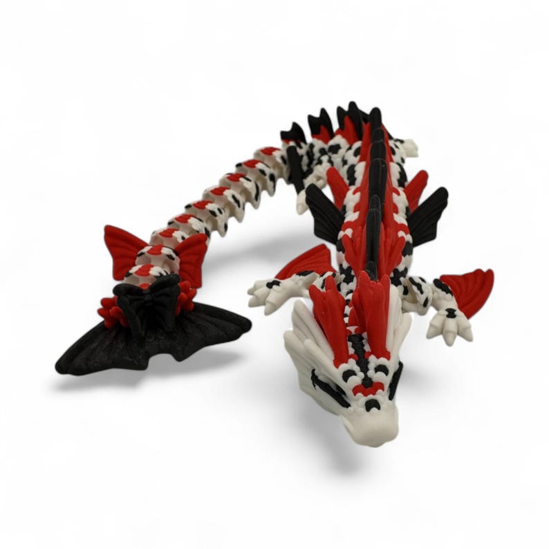 May include: A detailed, articulated dragon figurine in red, black, and white. The dragon has a long, segmented body, with fins and spikes. The head is white with black and red accents. The dragon is posed on a white background.
