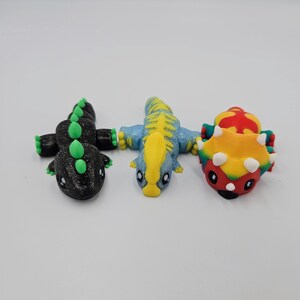 May include: Three small dinosaur figurines, one black with green accents, one blue with yellow accents, and one red, yellow, and green.