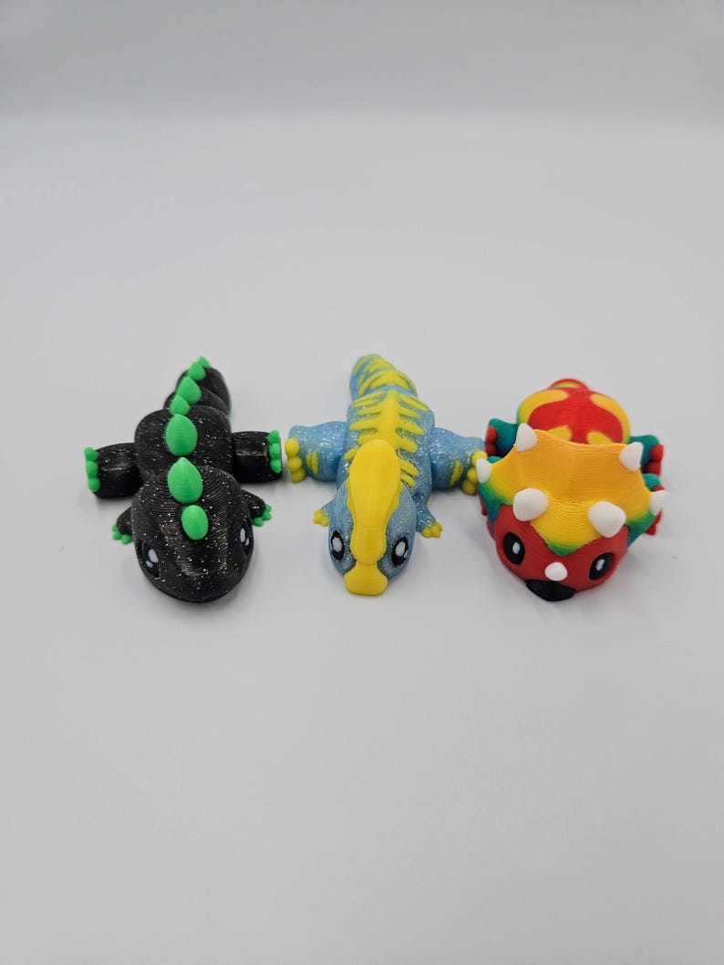 May include: Three small dinosaur figurines, one black with green accents, one blue with yellow accents, and one red, yellow, and green.