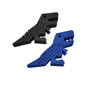 Puede incluir: Dos objetos con forma de dinosaurio, uno negro y otro azul, se muestran sobre un fondo blanco. Los dinosaurios tienen un dise&ntilde;o geom&eacute;trico, con una serie de peque&ntilde;os cuadrados que forman sus cuerpos y dientes irregulares.