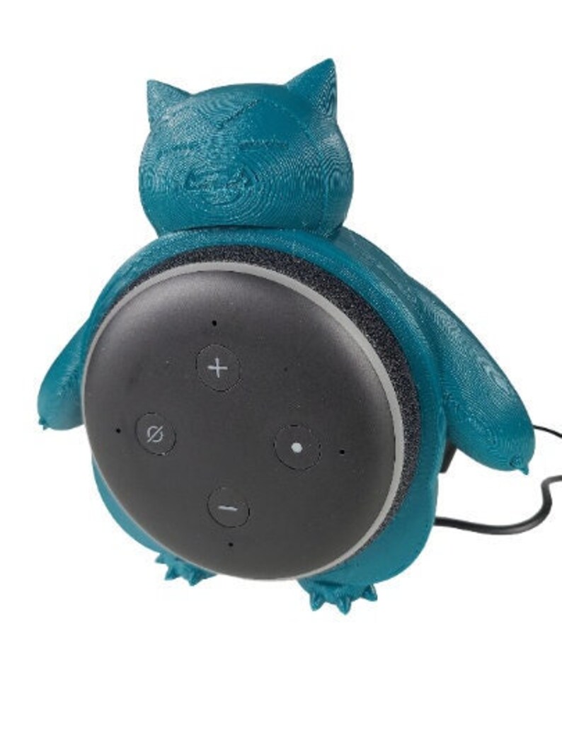 May include: A teal blue 3D printed  speaker stand shaped like a cartoon character. The stand is designed to hold a round, black smart speaker with four buttons.