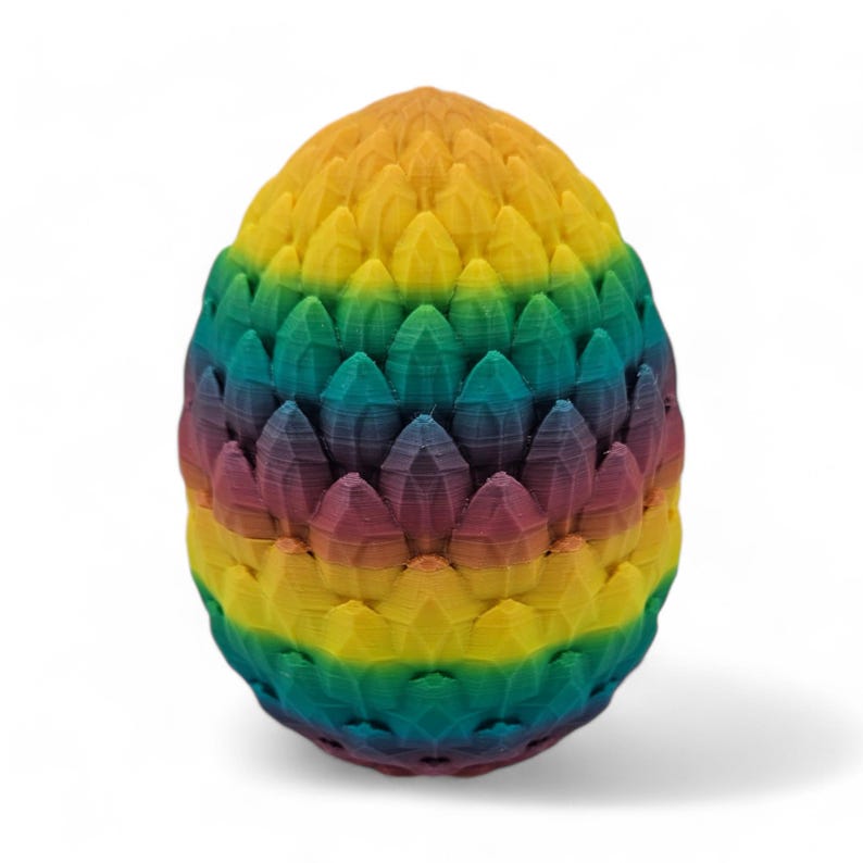 May include: A colorful, egg-shaped decorative object. The object is made up of layers of rainbow-colored, petal-like shapes. The colors transition from yellow to green, blue, purple, and red. The object is standing on a white surface.