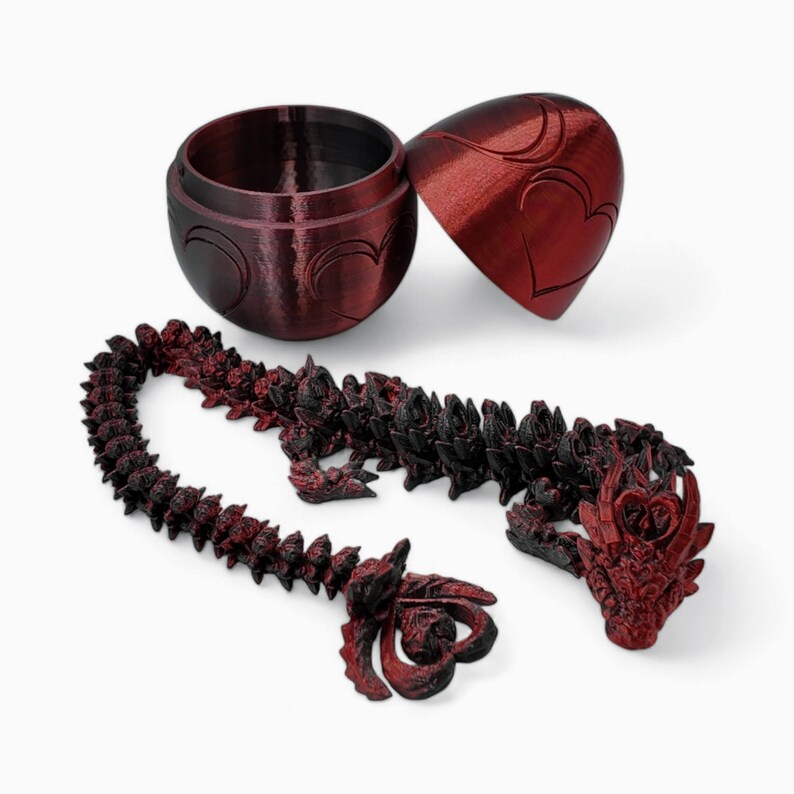 May include: A red heart-shaped egg-shaped box with a dragon-shaped necklace made of black and red beads. The necklace has a dragon head at each end.