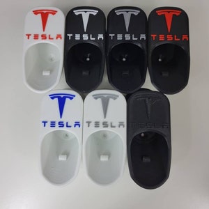 May include: Six white and black 3D printed Tesla key holders with the Tesla logo and text. The key holders are in various colors, including red, white, black, blue, and gray.
