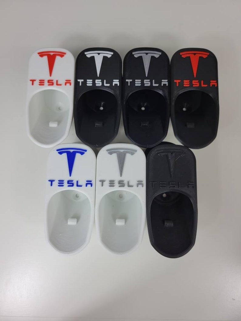 May include: Six white and black 3D printed Tesla key holders with the Tesla logo and text. The key holders are in various colors, including red, white, black, blue, and gray.