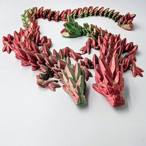 Peut inclure: Un dragon imprimé en 3D en plastique rouge et vert. Le dragon est enroulé en cercle, la tête et la queue se touchant. Le dragon est composé de nombreuses petites écailles pointues.