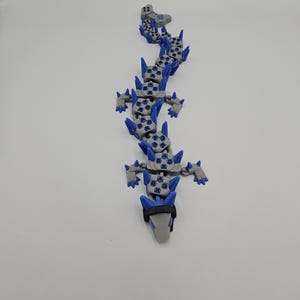 May include: A gray and blue articulated dragon toy. The dragon has a segmented body with blue accents and spikes. The head is gray with a black band. The toy is designed to be flexible and poseable.