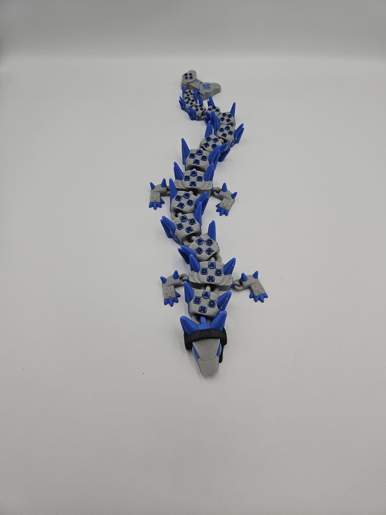 May include: A gray and blue articulated dragon toy. The dragon has a segmented body with blue accents and spikes. The head is gray with a black band. The toy is designed to be flexible and poseable.