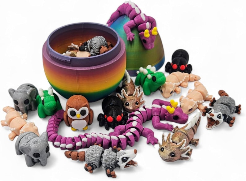 K&ouml;nnte beinhalten: Ein regenbogenfarbener eif&ouml;rmiger Beh&auml;lter mit Deckel, gef&uuml;llt mit kleinen Tierfiguren. Die Figuren umfassen einen lila Drachen, einen gr&uuml;nen Dinosaurier, eine braune Eule, einen grauen Elefanten, einen grauen Opossum, einen braun-wei&szlig;en Axolotl, einen grau-wei&szlig;en Opossum, einen gr&uuml;nen Frosch, eine braun-wei&szlig;e Eidechse, einen lila segmentierten Drachen, eine schwarze Spinne und eine beige Eidechse.