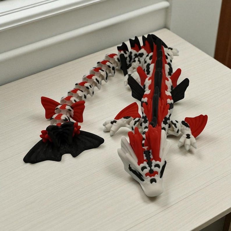 May include: A 3D-printed articulated dragon toy in red, black, and white. The dragon has a long, segmented body, with red fins and accents. The head is white with black details. The toy is designed to be poseable and flexible.
