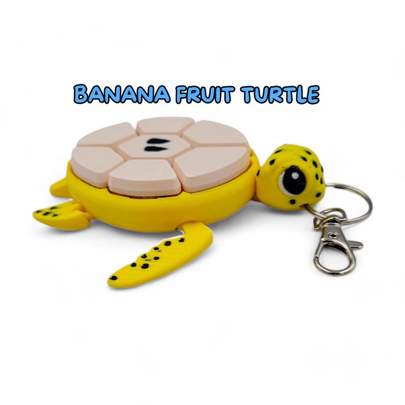 May include: A yellow turtle keychain with a pink and white banana fruit design on its shell. The keychain has a silver metal clasp.