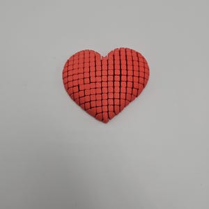 May include: A red heart-shaped object, constructed from small, square blocks. The heart is centered against a plain white background, with the blocks arranged to form the shape. The color is a vibrant, solid red.