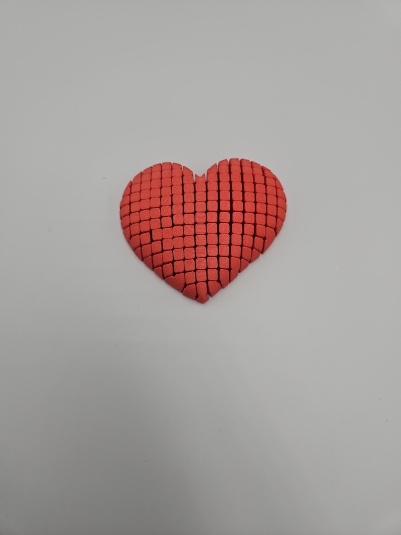 May include: A red heart-shaped object, constructed from small, square blocks. The heart is centered against a plain white background, with the blocks arranged to form the shape. The color is a vibrant, solid red.