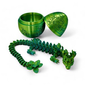 Pu&ograve; includere: Una statuetta di drago verde stampata in 3D con un design floreale. Il drago &egrave; composto da molti piccoli pezzi che si incastrano. Il drago &egrave; in una posizione arrotolata, con la testa che riposa sulla coda. Il drago &egrave; seduto su una superficie bianca.