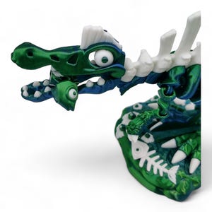 May include: A green and white plastic dinosaur toy with a skeleton design. The dinosaur has large eyes and is holding a fish in its mouth.