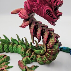 May include: A 3D-printed articulated dragon toy in shades of red, green, and blue. The dragon's head is a vibrant red, with intricate details. The body transitions to green and blue segments, creating a colorful, fantasy-themed collectible.