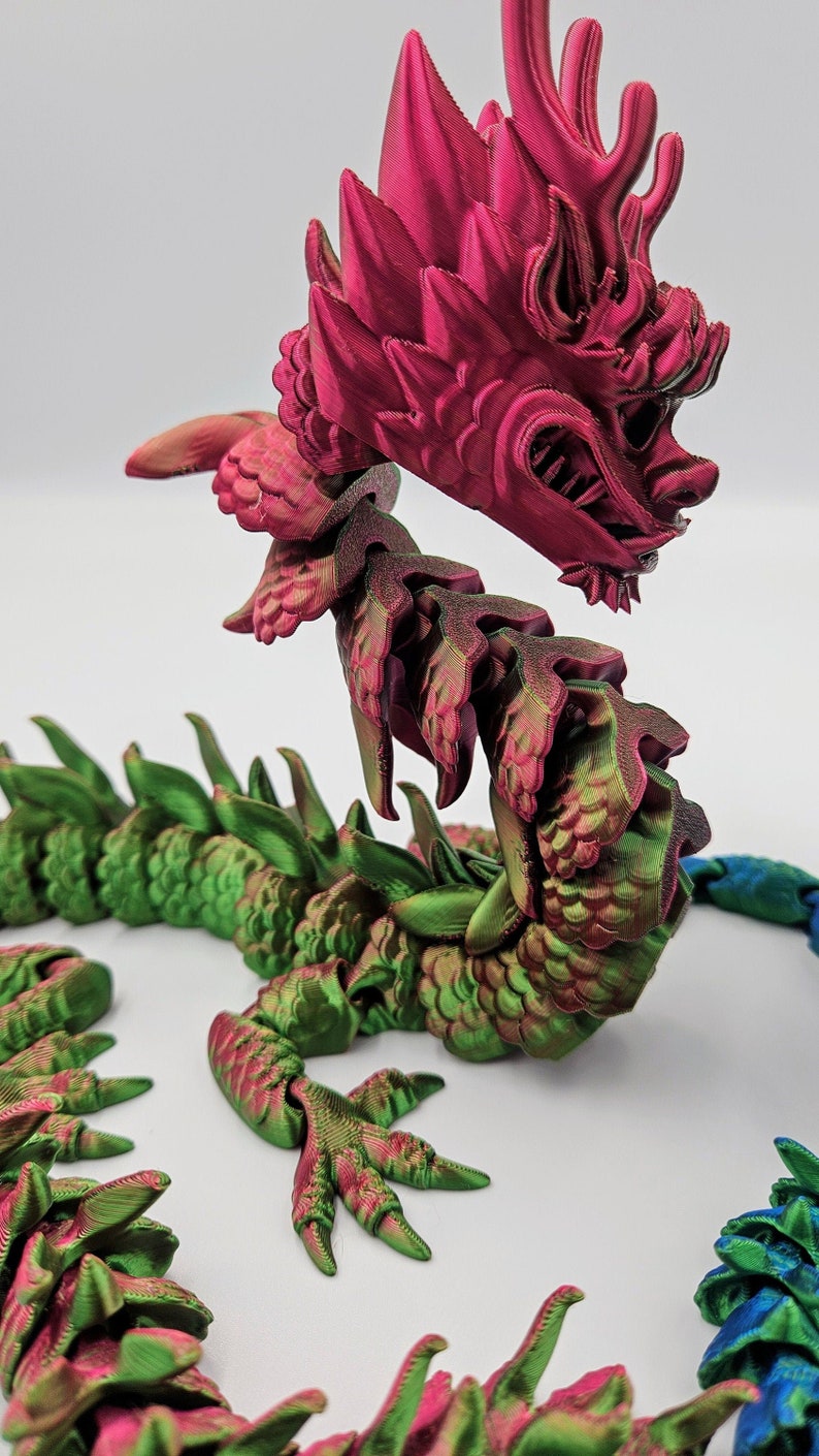 May include: A 3D-printed articulated dragon toy in shades of red, green, and blue. The dragon's head is a vibrant red, with intricate details. The body transitions to green and blue segments, creating a colorful, fantasy-themed collectible.