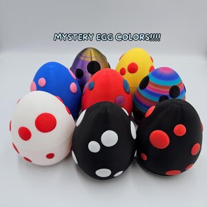 May include: Eight colorful speckled Easter eggs with a variety of patterns and colors, including red, white, black, blue, yellow, and purple. The eggs are arranged in a circle on a white surface. The text "MYSTERY EGG COLORS!!!" is written in blue letters at the top of the image.
