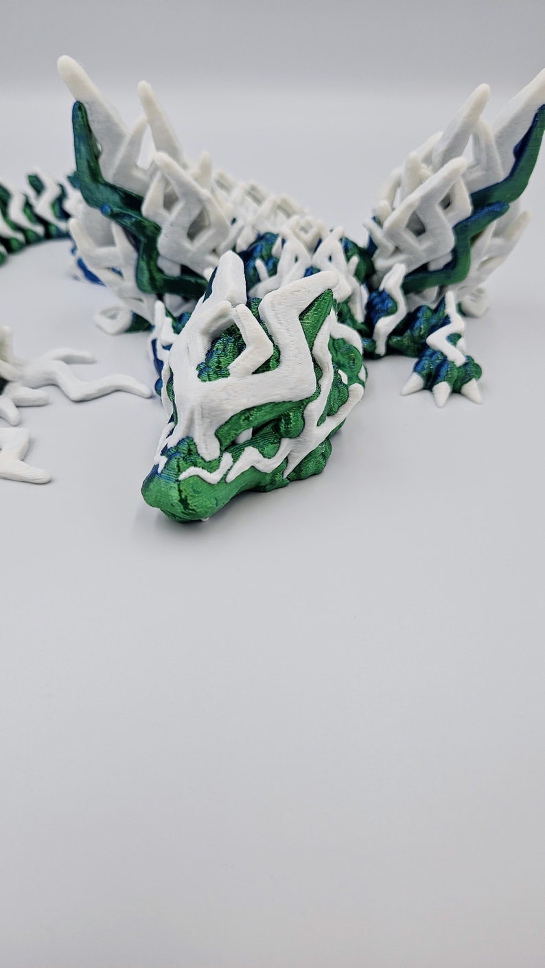 May include: A 3D printed green and white dragon figurine with intricate details. The dragon has a long tail and large wings.