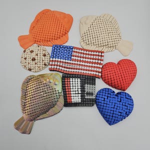 May include: An assortment of decorative items including an orange fish, a beige fish, a cookie, an American flag, a red heart, a blue heart, a metallic fish, and a black and white square.