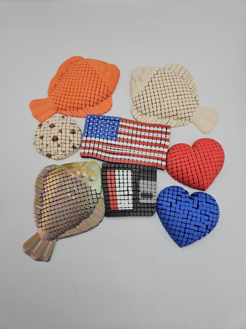May include: An assortment of decorative items including an orange fish, a beige fish, a cookie, an American flag, a red heart, a blue heart, a metallic fish, and a black and white square.
