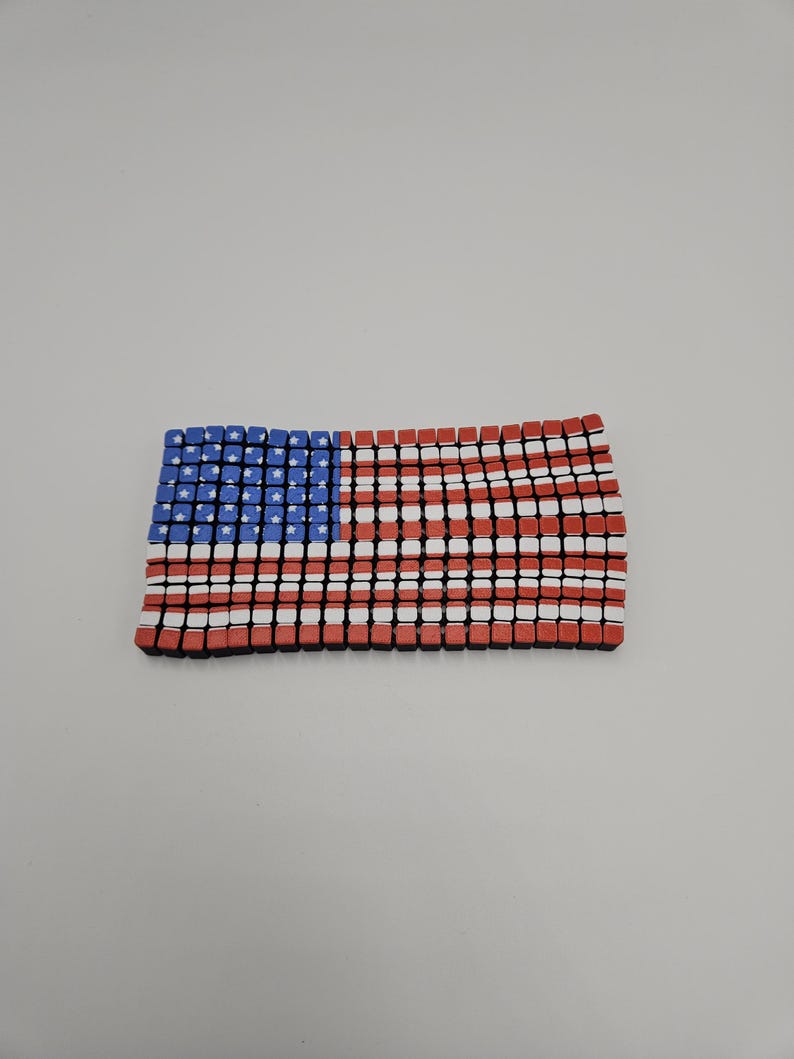 May include: A rectangular American flag design composed of small, colorful blocks. The flag features a blue field with white stars in the upper left corner and red and white stripes across the rest of the flag.
