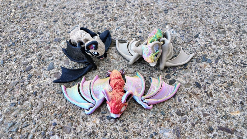 May include: Three small bat figurines with wings outstretched. One is black, one is beige with brown accents, and one is red with iridescent wings.