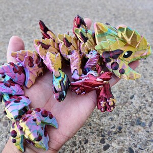 May include: A multi-colored, segmented, articulated, dragon-like toy made of plastic. The toy is painted in shades of red, pink, yellow, green, and blue. The toy has a textured surface and appears to be hand-painted.