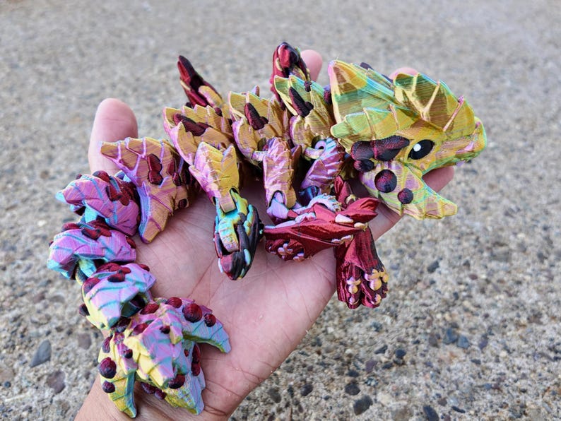 May include: A multi-colored, segmented, articulated, dragon-like toy made of plastic. The toy is painted in shades of red, pink, yellow, green, and blue. The toy has a textured surface and appears to be hand-painted.