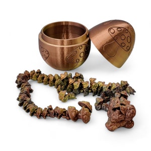May include: A copper-colored mushroom-shaped trinket box with a hinged lid. The box is open and a string of small copper-colored mushroom charms is spilling out.