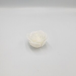 May include: A single, off-white, rose-shaped candle. The candle is unscented and has a detailed petal design. The candle is sitting on a white surface. The candle is likely used for home decor or special occasions.