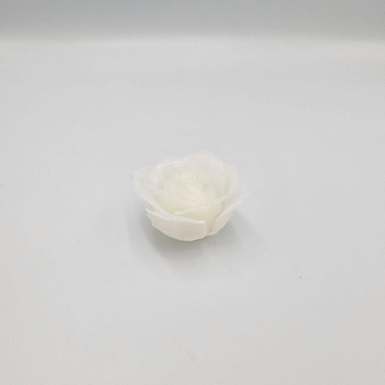 May include: A single, off-white, rose-shaped candle. The candle is unscented and has a detailed petal design. The candle is sitting on a white surface. The candle is likely used for home decor or special occasions.