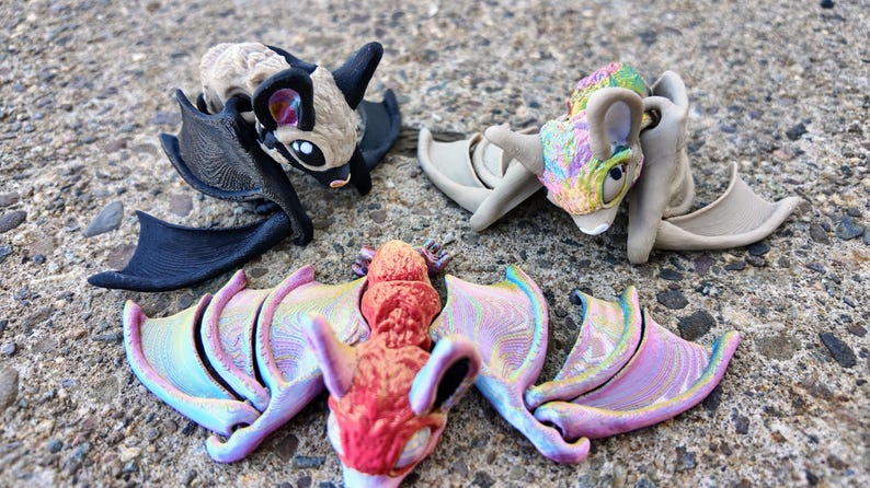 May include: Three colorful bat figurines with iridescent wings. The bats are made of plastic and have different colors and patterns.